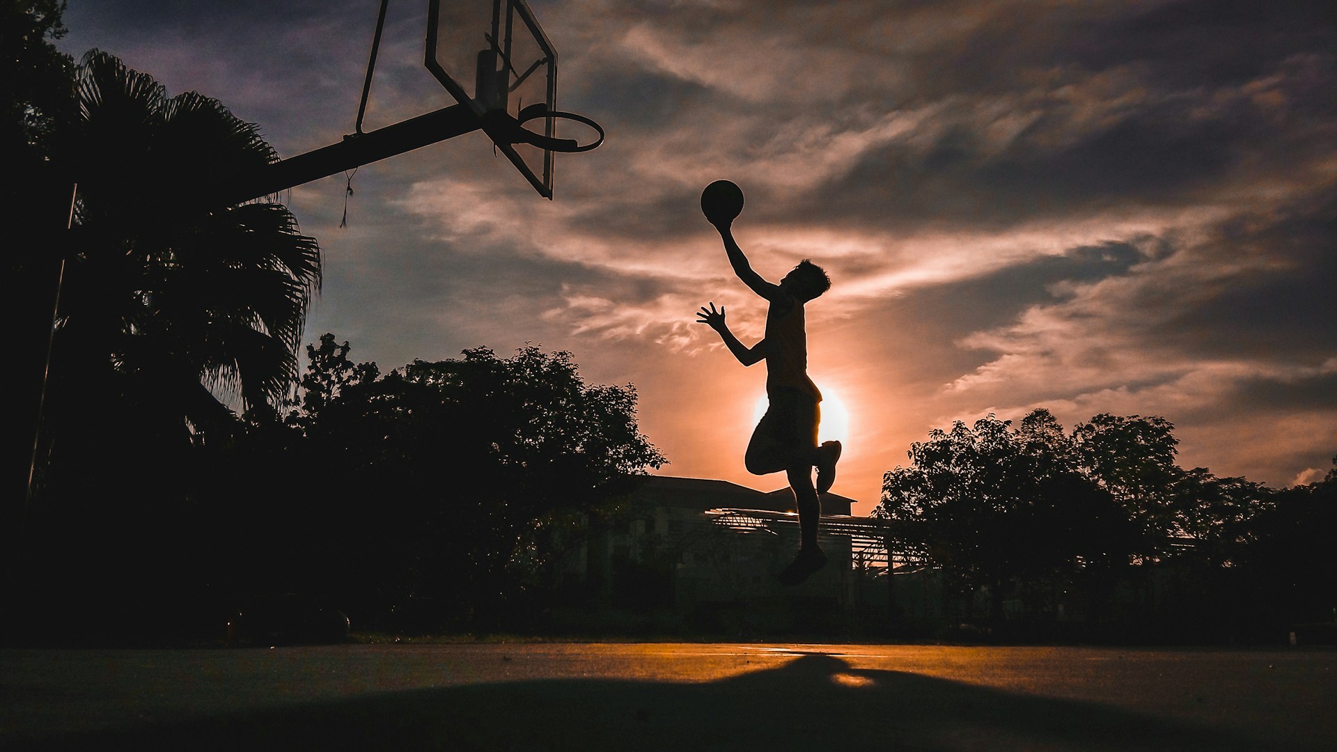 Silhouette of a basketball player going up for a dunk at sunset
